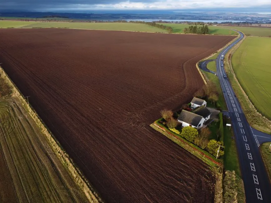 Aerial shot of expansive farmland with a cottage and road in rural Scotland.